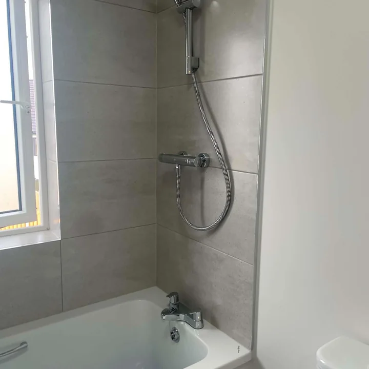 Bathroom renovation with bath, shower fittings and grey wall tiling